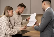 Co sprawdzić przed sprzedażą nieruchomości samodzielnie? Para w kuchni ogląda z doradcą dokumenty dotyczące mieszkania